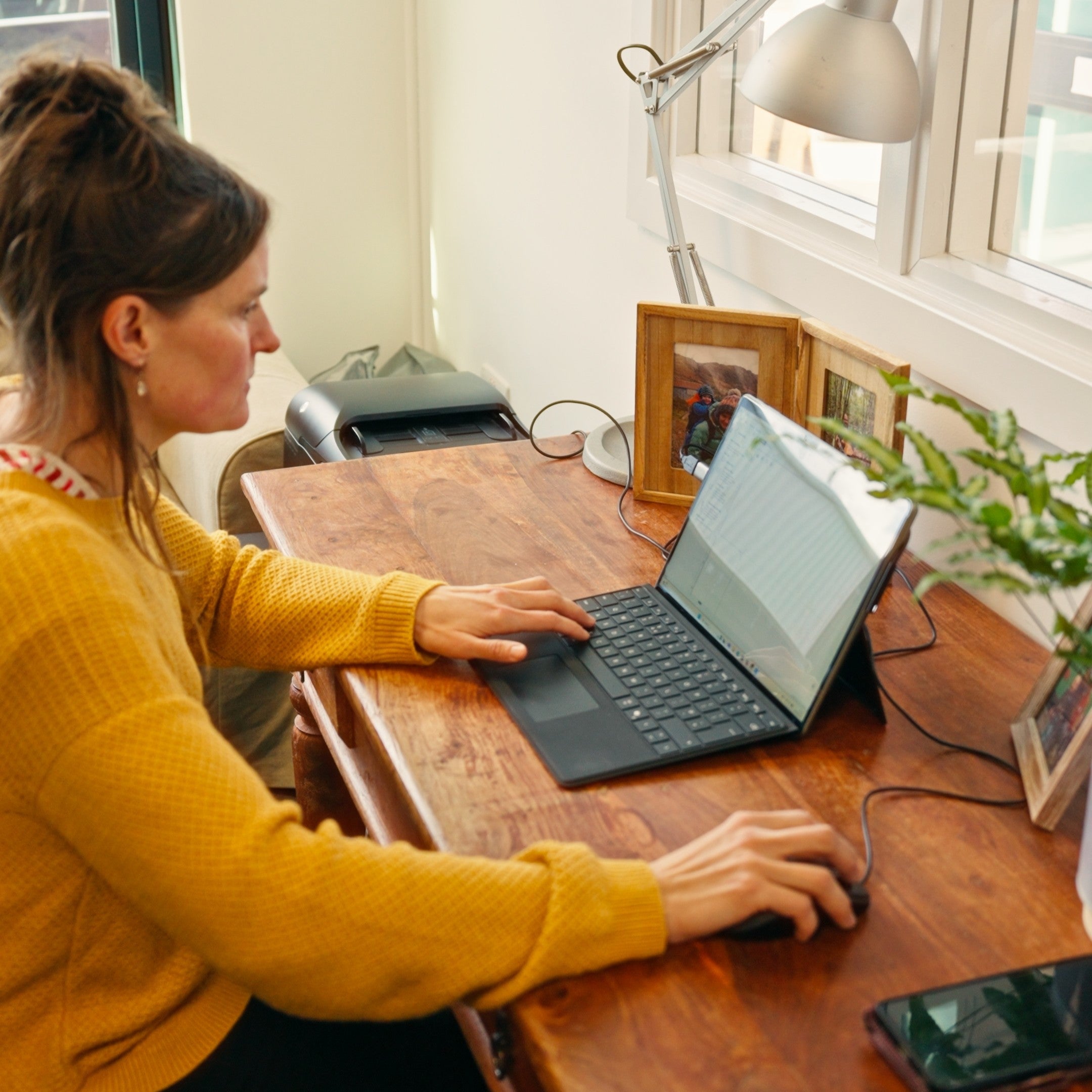 Person at a computer with family photos and a plant on desk